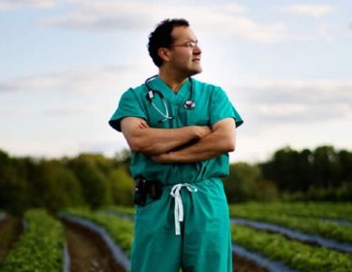 Dr Quinones standing in a farm field wearing his surgical scrubs